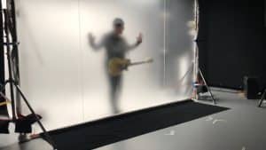 U2 band member behind a large diffusion screen, creating a ghostly silhouette while playing guitar for 2018 tour video, managed by Films.Solutions.