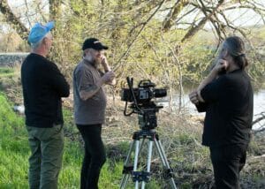 The director, DOP, and Lukas, engaged in a deep discussion near the site where the body was discovered in 1979, strategizing for the next scene.