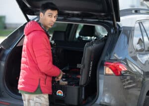Edward, the soundman, meticulously prepares for a day of work, selecting equipment from his travel case in the open trunk of his car.