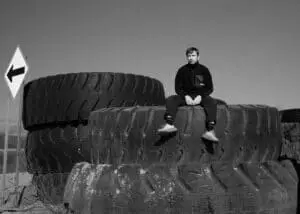 Black and white image of the cinematographer sitting on a giant tire of a mining truck