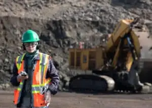 Client liaison officer in safety gear listening to the last take with a giant hydraulic mining shovel in the background