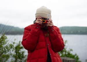 Client liaison officer capturing moments with a disposable camera, adorned in a red jacket and white hat during the Fay Archive filming expedition