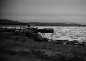 Black and white image of the team admiring large ice chunks in a bay, with a seemingly timeless village in the south of Labrador in the background