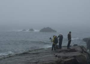 Cinematographer focusing on filming the harsh, wild sea, with the vast flat rock in the foreground
