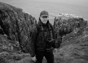 Black and white close-up of Richard, a renowned film fixer, standing by a cliff with the massive Bird Rock in the background