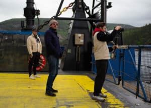 Cinematographer filming on the front part of a ferry, with Richard the Fixer and the Director, crossing the Saguenay River in Québec