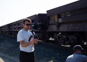 Concentrated cinematographer filming a moving train with a Sony camera on a gimbal, en route to Labrador City