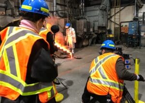 Filming crew capturing a mine employee pouring molten gold into molds.