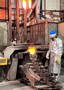 Mine employee in a heat shield suit pouring molten gold to create gold bars.