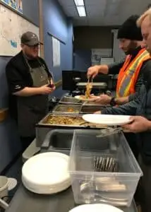 Technician filling his plate with a variety of dishes under the chef's supervision.