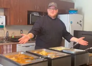 Chef standing with a welcoming smile, array of delectable meals laid out in front.
