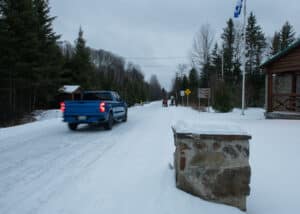 View from behind of a blue Chevrolet pickup truck entering the gates of Parc d'Aiguebelle, Quebec with the film crew in the background.
