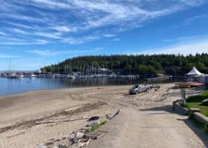 A scenic view of Tadoussac beach with a harbor and numerous private boats in the background during location scouting.